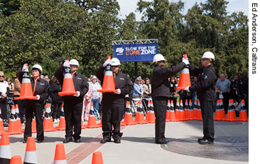 Figure 2. Photo. Five members of the Caltrans Honor Guard dedicate four traffic cones at the National Work Zone Awareness Week kickoff event in Sacramento, CA, on April 8, 2008. Three cones represent the Caltrans workers killed in work zones in 2007, while a fourth cone commemorates all fallen highway workers across the Nation. Members of the crowd attending the event can be seen behind the Honor Guard.
