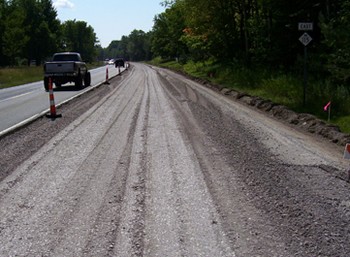 Figure 3. Photo. A close-up view of M-115 in Clare County, Michigan. One side of the two-lane roadway is closed for paving, while traffic travels in the other lane.