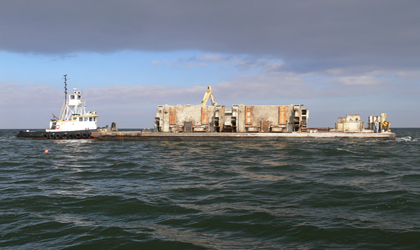 Photo. Steel drawbridge trunnions from the old Woodrow Wilson Bridge outside of Washington, DC, are hauled by barge to the Point No Point Reef near the mouth of the Potomac River.