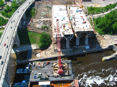Figure 6. Photo. An aerial view showing construction of the new Interstate 35W bridge in Minneapolis, Minnesota. The superstructure for the new bridge is being built. To the left, traffic travels across an adjacent bridge.