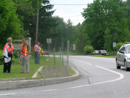 Photo. A road safety audit is conducted on US 4 in Quechee, VT. A car is partly visible rounding the corner on the roadway. Four participants in the audit are standing on the side of the roadway.