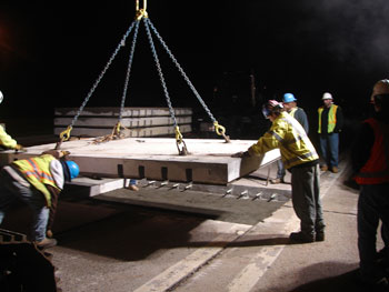 Figure 6. Photo. Workers position a precast concrete pavement slab as it is lifted into place on I-295 in New Jersey in 2008.