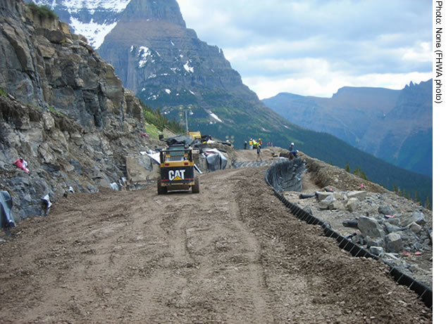 A mechanically stabilized earth wall under construction in Montana's Glacier National Park. Construction equipment is visible in the foreground. Mountain peaks are in the background.