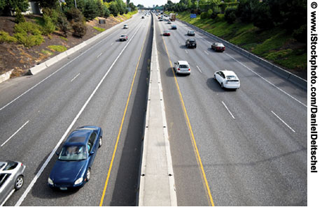 An overhead view of a highway. Three lanes of traffic are traveling in both directions.