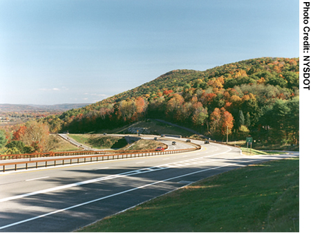 A ground-level view of a highway winding away next to a tree-covered hill.