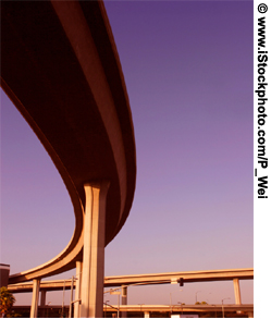 A view of the underside of a curving highway overpass span.