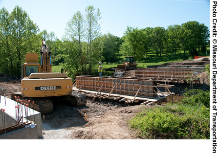 A view of a bridge under construction over Spring Creek in Cole County, MO. Construction equipment is in the foreground. The bridge was replaced under the Missouri Department of Transportation's Safe and Sound Bridge Improvement Program.
