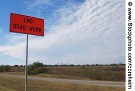 A sign reading "End Road Work" is seen in the foreground, with fields and blue sky in the background.