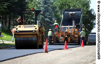A close-up shot of a work crew operating machinery to pave a road. Six workers are visible.