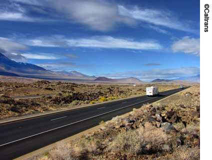 U.S. Route 395 in Inyo County, California, which was converted from a two-lane highway to a four-lane expressway. An RV is seen traveling on the expressway. Native landscaping surrounds the roadway.