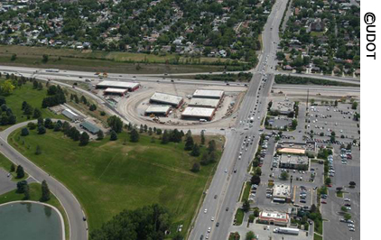 An aerial view of seven prefabricated bridges built offsite by the Utah Department of Transportation at its "bridge farm." The bridges are now ready for shipping to their destination. Running next to the "bridge farm" is a roadway with three lanes of traffic traveling in each direction.