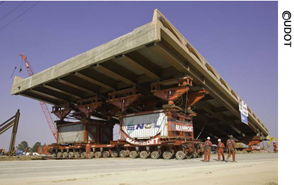 A view of a self-propelled modular transporter hoisting the 4500 South bridge in Salt Lake City, Utah, in 2007. Three workers are visible in the foreground.