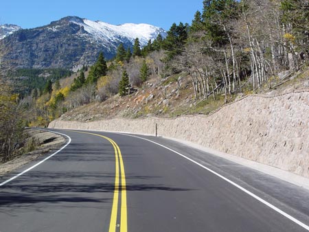 Figure 6. Photo. A road in Rocky Mountain National Park near Estes Park, Colorado. On the right-hand side of the roadway is a soil nail earth retaining structure built by the Federal Highway Administration's Central Federal Lands Highway Division. In the background are snow-covered mountain peaks.