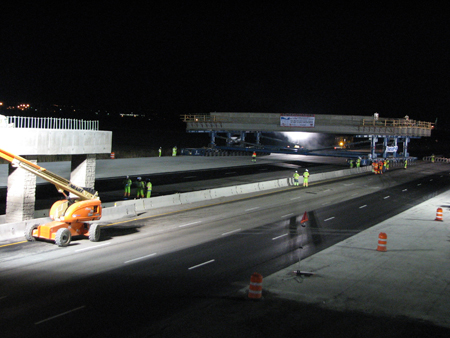 A night-time view of the Proctor Lane bridge under construction in Utah County, Utah. In the background is the new prefabricated bridge superstructure. Workers can be seen in the foreground