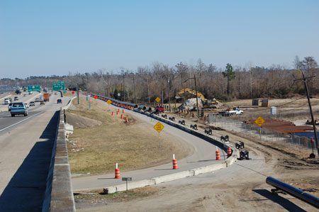 A view of a roadway construction site, where utilities are being relocated as part of the Interstate 10 bridge replacement project over the Neches River in Texas. Trucks and other construction equipment are in the background.