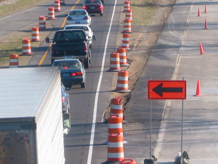Figure 6. Photo. Traffic travels through a work zone. The right side of the roadway is blocked off with barrels, while a sign with an arrow directs traffic to the left lane.
