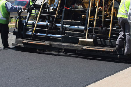 A close - up of asphalt paving equipment being used to pave a road.