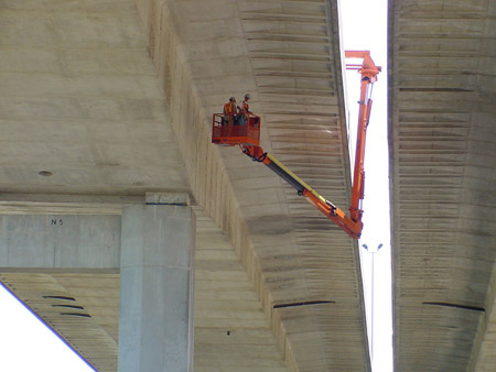Two workers in an under-bridge inspection vehicle conduct a bridge inspection in Michigan.