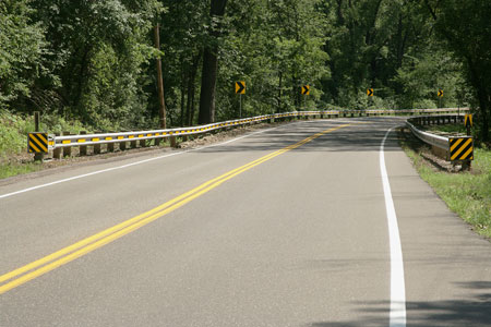 A close-up view of a white pavement marking on a rural roadway. The road is using the All-Weather Pavement Marking System, which makes it easier for drivers to see markings on wet roads.