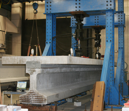  A close-up view of ultra-high performance concrete composite connection test specimens being subjected to cyclic loading in a laboratory. The specimen is seen in a load frame undergoing the testing.