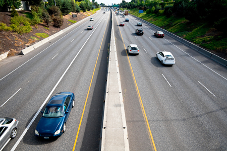 An overhead view of a highway. Three lanes of traffic are traveling in both directions.