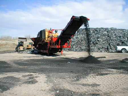 Shingles are processed for recycling. Machinery dumps the shingles into an outdoor stockpile.