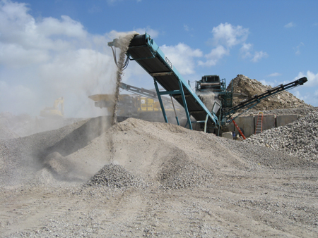 Concrete is processed for recycling. Machinery dumps the concrete into an outdoor stock pile.