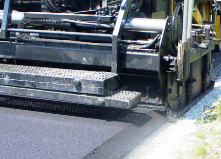 A close-up view of an asphalt paver using the Safety Edge paving technique, which shapes the edge of the pavement to approximately 30 degrees.