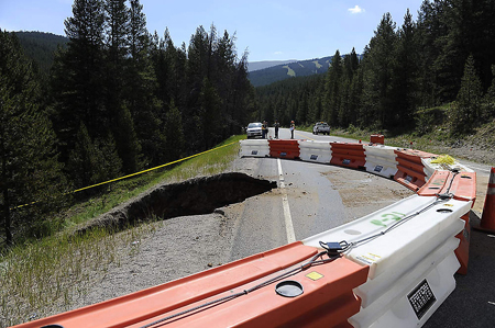 In the foreground yellow tape and jersey barriers block off a damaged culvert and adjacent embankment that have failed near the Eisenhower Tunnel in Colorado. In the background are four workers standing near the damaged area.