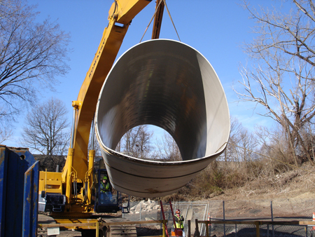 A close-up of a steel culvert being hoisted in the air by a crane.