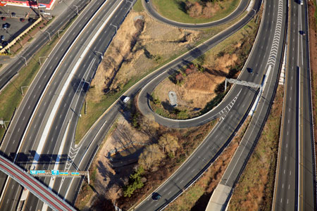 An aerial view of a highway interchange, with three separate roadways to the right and four to the left.
