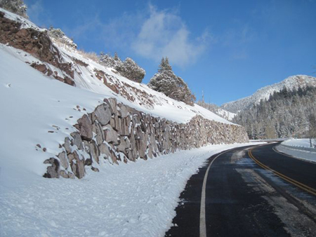 A view of Beaver to Junction Highway in southern Utah in winter. To the left of the highway is a snow-covered slope that ends in a rockery at the bottom of the slope containing stacked angular rocks.