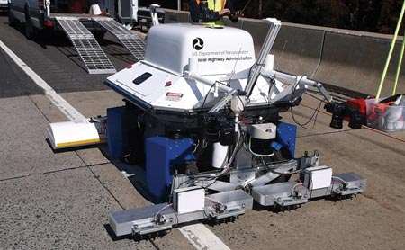 This image shows the RABIT™ bridge deck assessment tool sitting on the NJ Rt. 55 over Porchtown Road steel multigirder cluster bridge. In the background, a large transport truck and an assessment team member are visible.