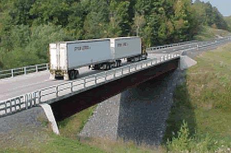 In this image, a double tractor trailer crosses a bridge. Due to the two attached trailers, the length of the truck nearly matches the length of the bridge.