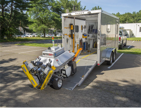 This photograph shows the RABIT™ (Robotic Assisted Bridge Inspection Tool) exiting from the systems operations center, which is a trailer attached to a pickup truck. The systems operations center is used to store equipment and transport the RABIT.