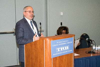 This photograph shows Dr. Jean Nehme standing at a podium giving a speech.