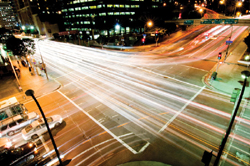 Photo. Urban, multilane intersection shown at night with streaks of light from transversing vehicles.