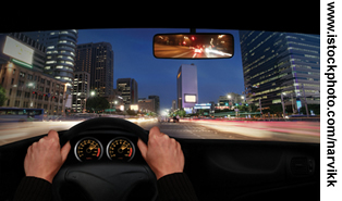 View from behind the wheel of a car driving through a city at night.