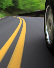 Photo. View of a two lane highway, double yellow centerlines, and left front wheel of vehicle on the road.