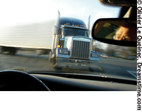 Photo. A driver’s eye view of an oncoming truck with the driver’s reflection seen in the mirror.