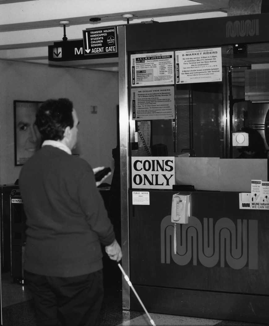 Figure 6. Photo. A traveler with a cane uses a RIAS device at a transit station.