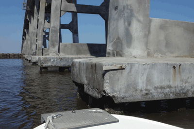 Photo. A closeup of cracked and spalled concrete at the foot of a bridge pier just above the water level (Herbert C. Bonner Bridge, Dare County, North Carolina).