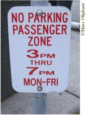 A close-up photo of a white traffic sign with red letters mounted on a metal pole. The sign reads: “No Passenger Zone; 3 p.m. thru 7p.m. Mon-Fri”.
