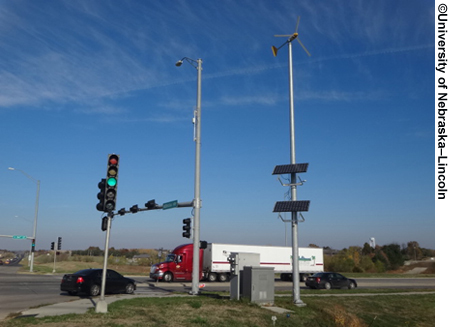 The renewable infrastructure in place. A truck is shown passing through an intersection which features a pole equipped with solar panels and a wind-powered device on top.