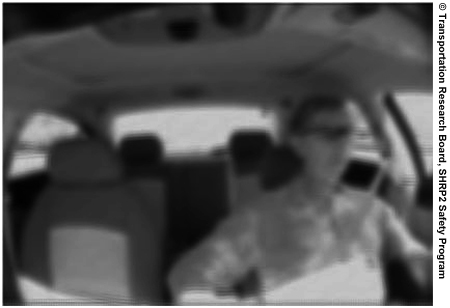 Figure 3. Photo. An intentionally blurred interior view of a vehicle looking back at the driver from the rear-view mirror.