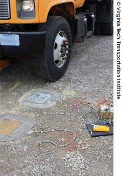 A photo shows a truck stopped in front of sensor pads embedded in the ground. Wires connect the pads to equipment placed on the ground next to the truck.