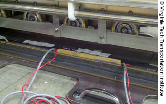 Figure 2. Photo. A truck is stopped in front of sensor pads embedded in the ground. Wires connect the pads to equipment placed on the ground next to the truck.