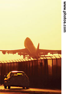 Figure 2. Photo. Moving away from the camera, a commercial airplane takes off from a runway with a car driving in parallel on the other side of the fence.
