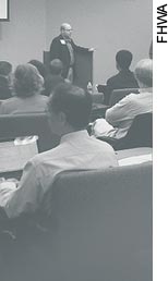 A view from the back of a workshop shows workshop participants as they listen to a presenter at the front of the room.