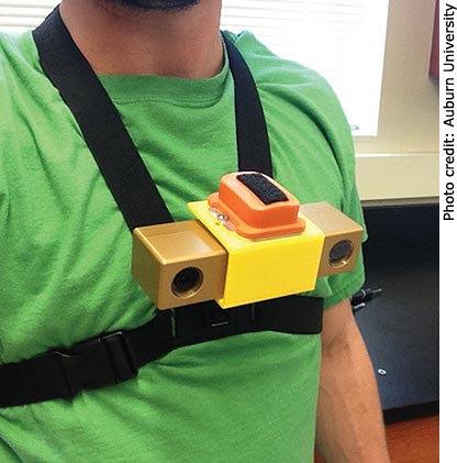 A close-up photo of a man in a green t-shirt wearing a chest-mounted device.